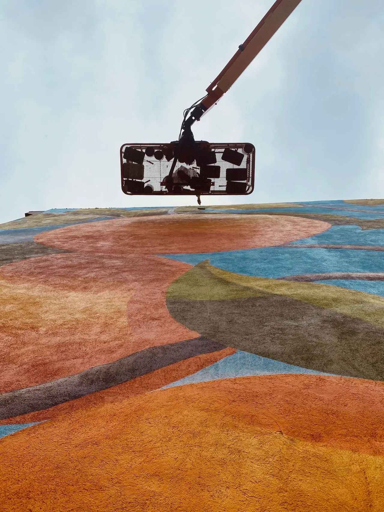 A paint roller on an extension pole above the mural, seen from the lift