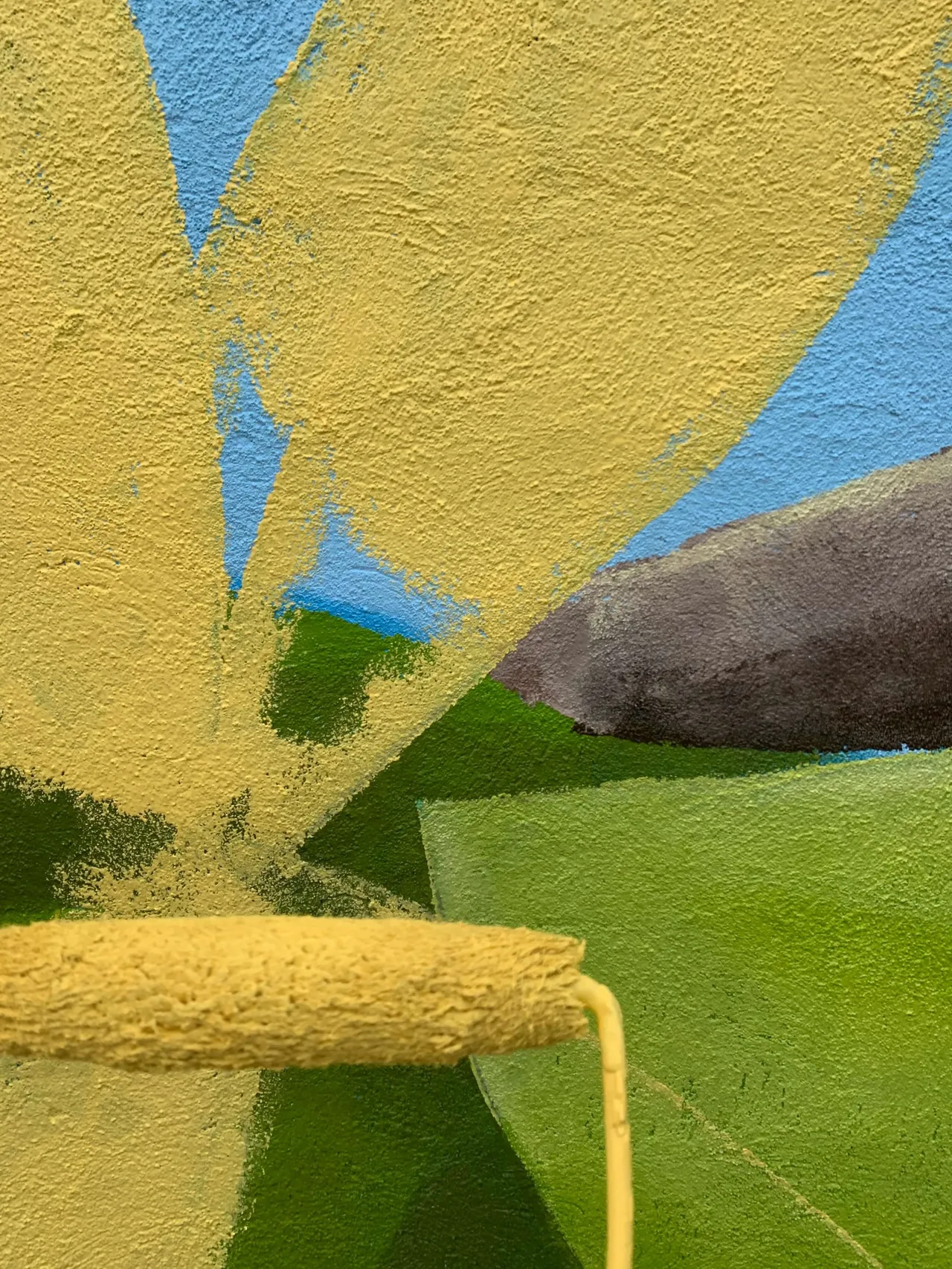 Close-up of a roller laying yellow paint onto a leaf