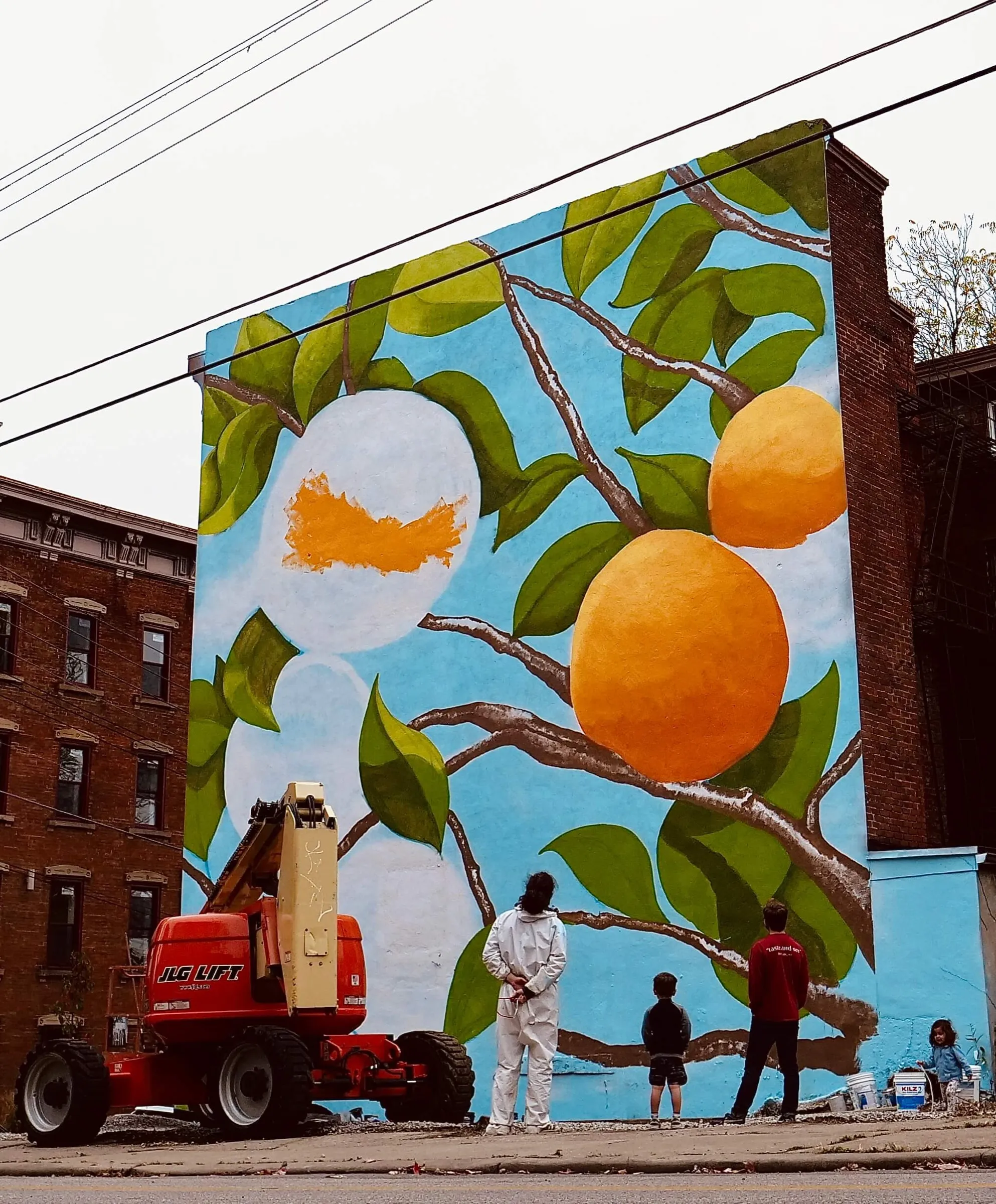 The mural in progress, with people watching from the sidewalk below